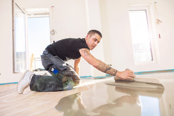 male worker working with self-levelling cement mortar during floor renovation