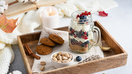Fototapeta na wymiar Blueberry dessert, cheesecake, trifle, mousse in a glass on a wooden tray with pistachios and oatmeal cookies. Side view. Cozy autumn composition. Confectionery