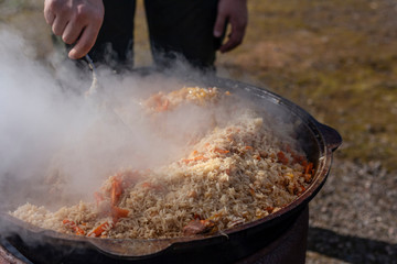 Rice in a cauldron. Cooking rice with meat on an open fire. Delicious food prepared in the fresh air. Rice stewed with vegetables. Shooting in natural light.