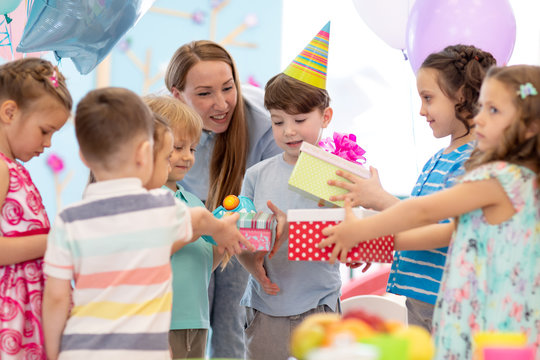 Childhood, holidays, celebration, friendship and people concept. Happy children in party hats giving gifts at birthday party