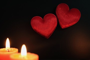 Two hearts with light candle on black background