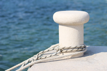 White mooring rope with knotted end tied around a cleat on a cement pier, boat lanyard.
