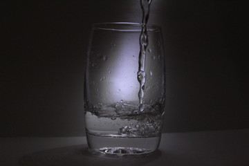 Water falling into the transparent / white glass with black background with some light