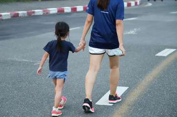 Fototapeta premium Closeup of Asian woman and girl walking together in jogging track on the street. Lovely and healthy family activity. 