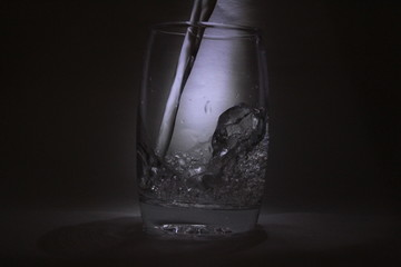 Water falling into the transparent / white glass with black background with some light
