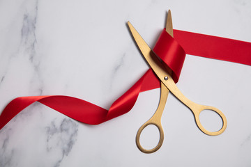 Grand opening background. Gold scissors with red ribbon on a marble background