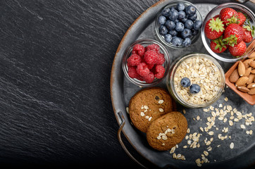 Flat lay view at vintage tray with ripe organic bilberry raspberry strawberry oat cookies and almonds set on slate closeup