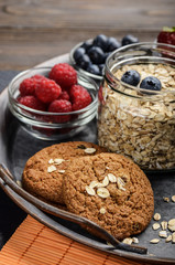 Tray with ripe organic bilberry raspberry strawberry oat cookies and almonds set on slate closeup