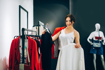 Black or white? Beautiful young woman trying to choose clothes to herself or customer while working...