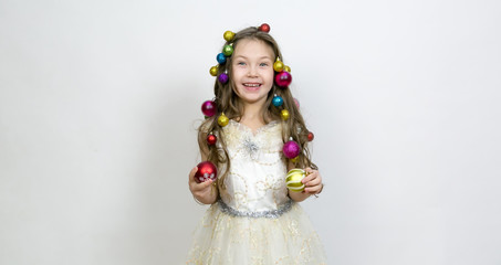 Girl with New Year's toys on a white background. A little girl with Christmas balls decorated hair on her head.
