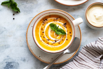 Yellow carrot or pumpkin soup with bread and sour cream on white marble background. Copy space....