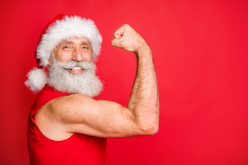 Naklejka premium Close up photo of cheerful santa claus in hat cap with white hairstyle showing his biceps gymwearing sportswear isolated over red background