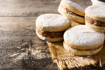 Traditional Argentinian alfajores with dulce de leche and sugar on wooden table. Copy space