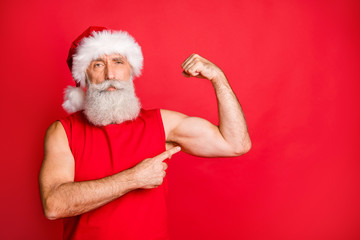 Portrait of confident santa claus in cap hat showing his triceps gym training effect wearing trendy...
