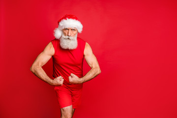 Fototapeta premium Full size photo of cheerful santa claus in hat showing his biceps cap smiling wearing panties sportswear isolated over red background