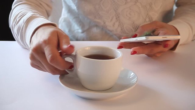 Cropped image of young woman sitting at a table with a coffee or tea and using mobile phone.