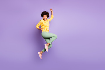 Full body photo of delighted afro american girl celebrate autumn spring jackpot victory raise fists scream yeah wear yellow sweater green pants trousers isolated over violet purple color background