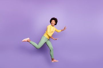 Fototapeta na wymiar Full size profile side photo of cheerful excited wavy hair girl jump run play catch-up game with friends on spring time wear yellow pullover green pants isolated violet purple color background
