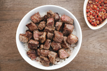 Homemade Bowl of Diced Beef Steak with rice and Thai style sauce on wooden table.