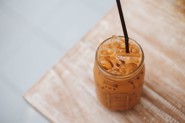 Iced Thai Milk Tea in glass with straw on wooden table in cafe.