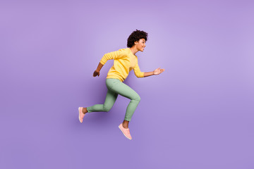 Fototapeta na wymiar Full body profile side photo of positive brunette curly hair dark skin girl hear news fall spring discounts jump run wear yellow pullover green pants trousers isolated violet purple color background