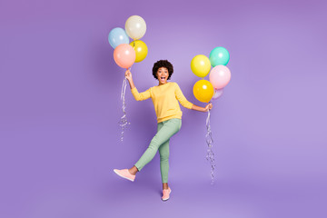 Fototapeta na wymiar Full size photo of funky funny teen girl hols many colorful baloons feel content crazy on spring holidays wear green sweater green pants trousers isolated over violet purple color background