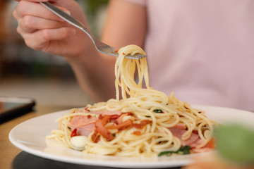 close up hand holding spaghetti noodle with ham spicy Italian food with white dish 