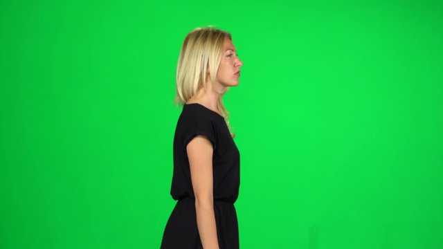 Pensive woman is walking on a green screen at studio. Side view