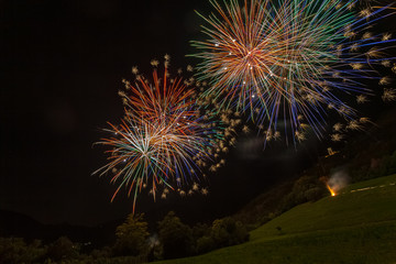 Brilliant and colorful fireworks above a wooded hill and against the backdrop of the night sky,...
