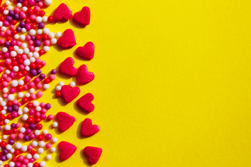 Small candies in the shape of hearts and balls are on a yellow background. Colorful candies over yellow background with a lot of space for text. Food, holidays, Valentines day  concept.