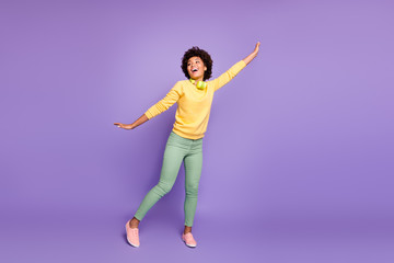 Fototapeta na wymiar Full size photo of cheerful positive afro american girl hold hands imagine she can fly like bird after listen music on wireless headset wear stylish outfit isolated violet purple color background