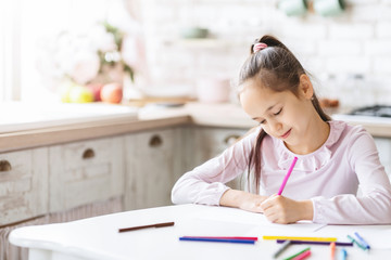 Cute little girl sitting in kitchen and drawing