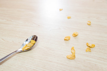 A metal spoon and cornflake cereal on a wooden surface