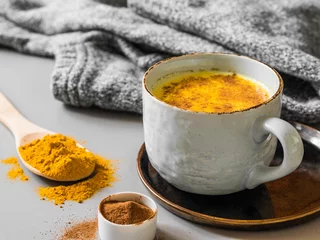 Kurkuma-Latte mit Milch und Zimt. Elixier der Gesundheit und Lebhaftigkeit. Traditionelles gesundes indisches Entgiftungsgetränk. Grauer Hintergrund © Anton Belo