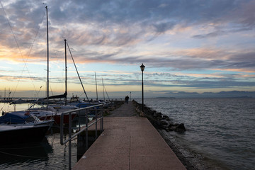 Obraz premium Pier at sunset on the lake Garda in Italy. Colorful sky and dramatic clouds
