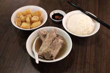 Bak Kut Teh served with rice and char kway (strips of fried dough) in a white bowl.