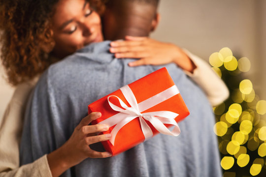 Loving afro woman hugging husband, holding christmas gift