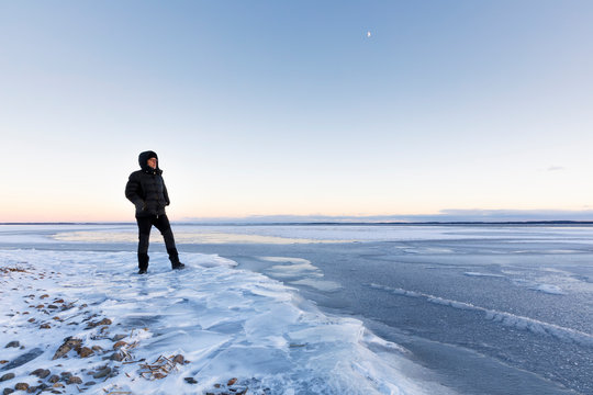 Man standing on frozen Glan lake at sunset in Ostergotland, Sweden