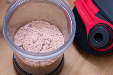 Chocolate whey protein powder a plastic shaker on wooden background.