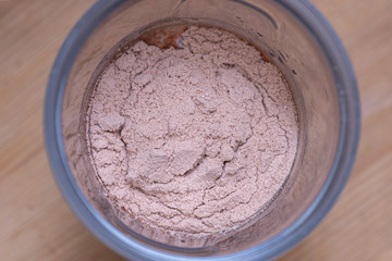 Chocolate whey protein powder a plastic shaker on wooden background.