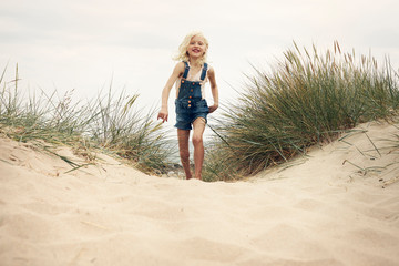 Girl wearing denim overalls walking on sand dune