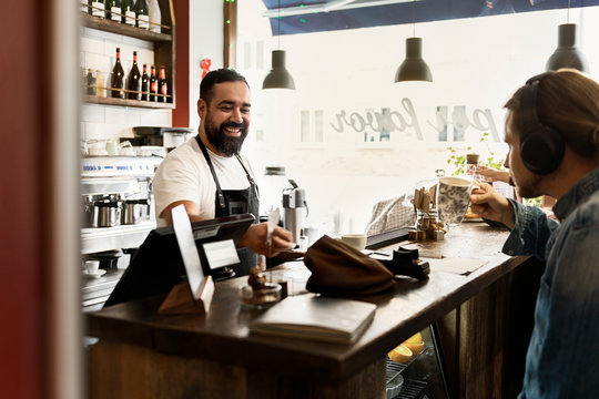 Smiling barista serving young man in cafe