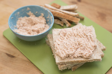 Preparing a tuna mayo sandwich on a chopping board. Wheat bread and tuna mayonnaise ready on the chopping board.
