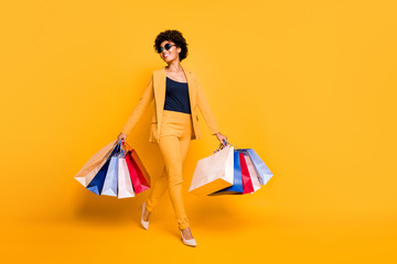 Full size photo of positive cheerful girl have leisure time feel dream dreamy hold bags go from shopping center wear style blazer trousers stilettos isolated over yellow color background - obrazy, fototapety, plakaty