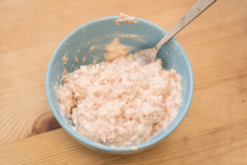 Tuna chunks in a bowl being mixed with mayonnaise. Preparing a tuna mayo sandwich on a wooden table.