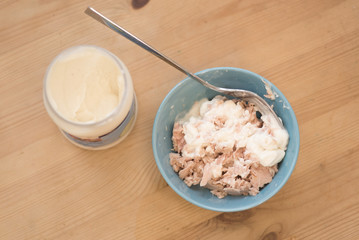 Tuna chunks in a bowl being mixed with mayonnaise in a jar. Preparing a tuna mayo sandwich on a wooden table.