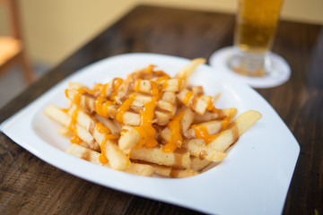 French Fries with Gravy and Melted Cheese on a white plate with a pint of beer on the background.
