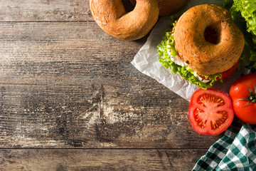 Vegetable bagel sandwich with tomato, lettuce, and mozzarella cheese on wooden table. Top view....