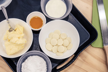 Sugar, butter, cream and white chocolate chips in a bowl for melting, preparing ingredients to make a cake.