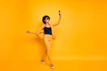 Fototapeta na wymiar Full body profile side photo of cheerful wavy hair girl have fun on leisure time go take selfie feel content wear style trousers sunglass blazer high-heels isolated yellow color background